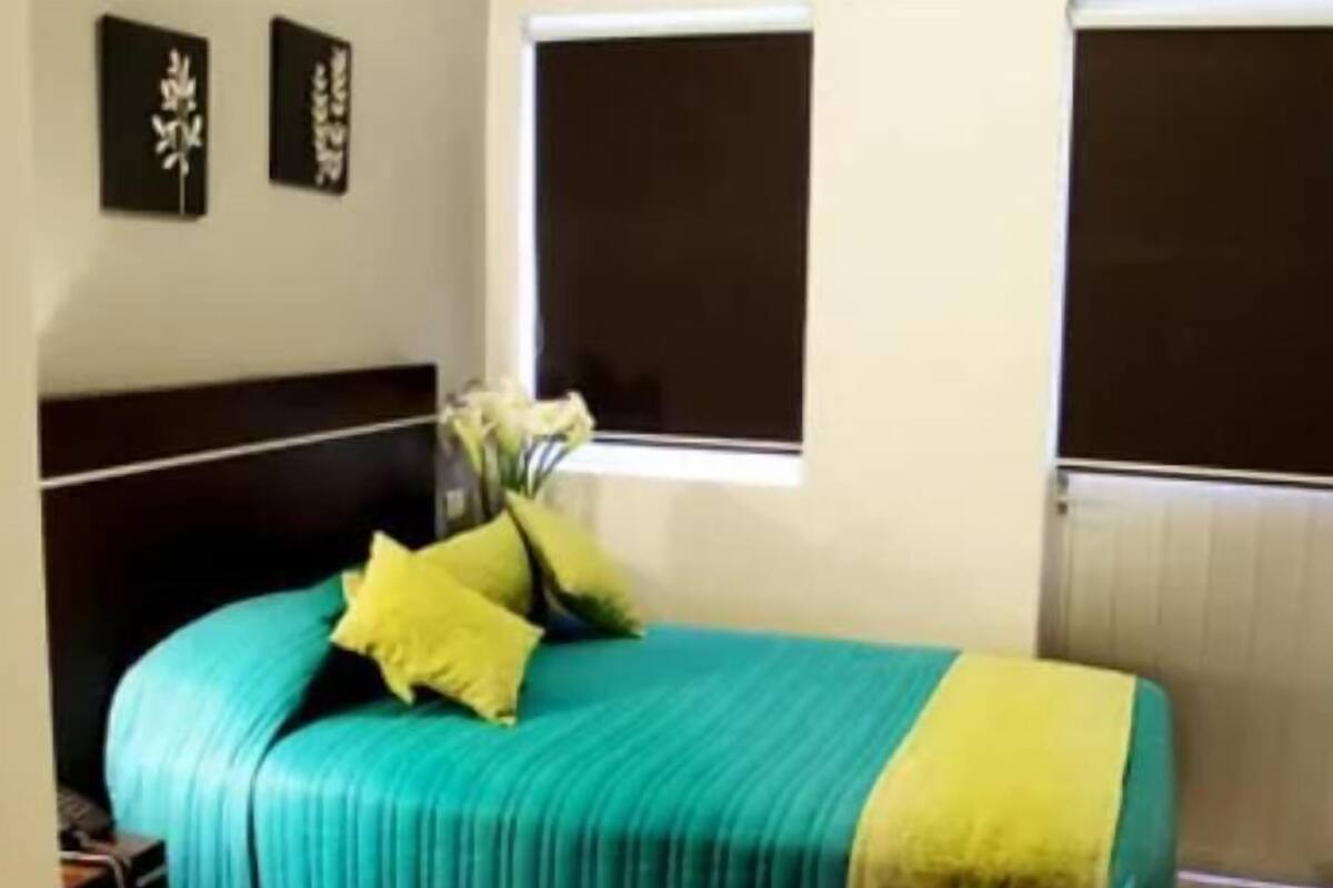 A bed with a teal and yellow bedspread, two pillows, and a vase with flowers on a nightstand.
