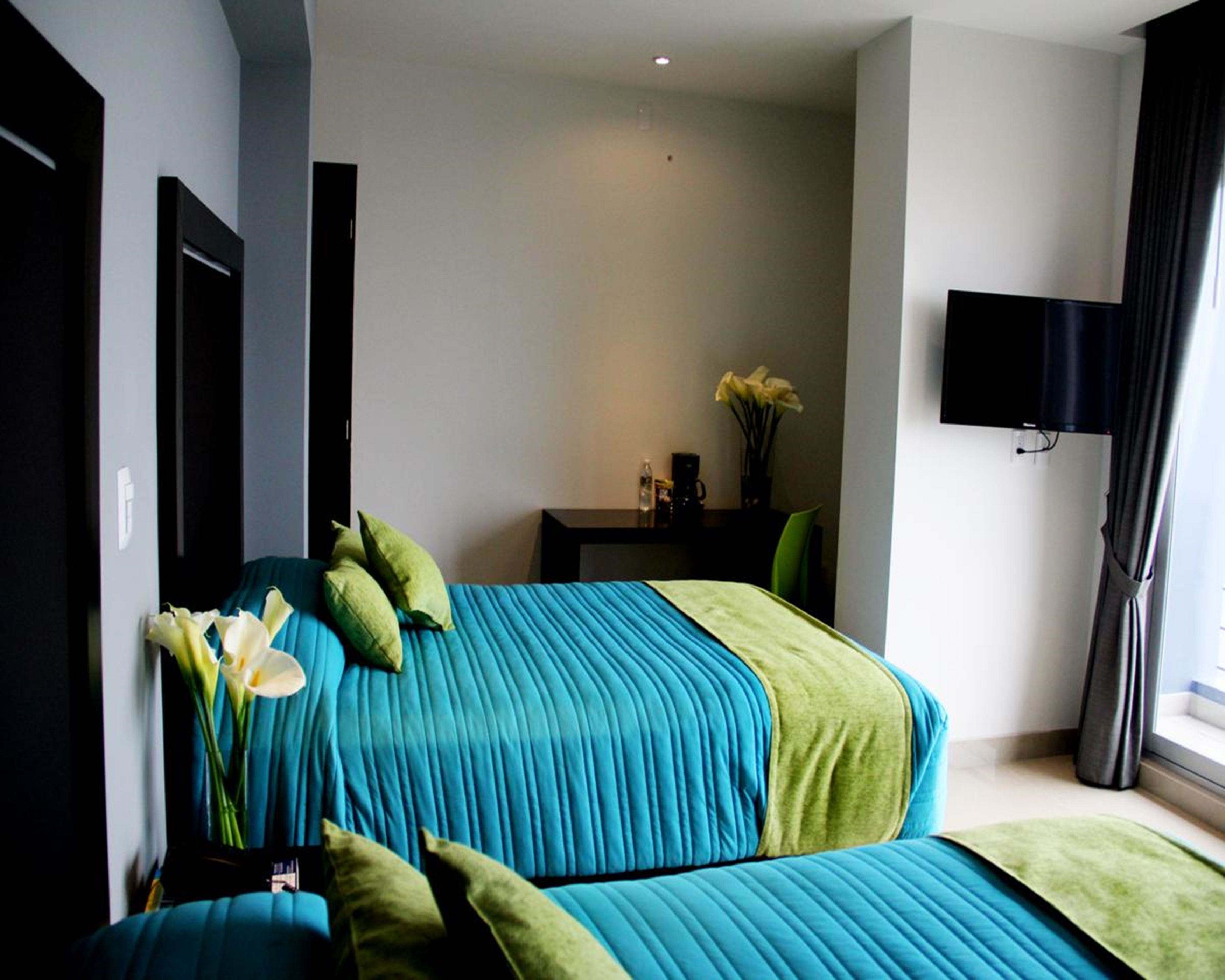 A modern bedroom with a large bed, a small table with a vase of flowers, and a TV mounted on the wall.