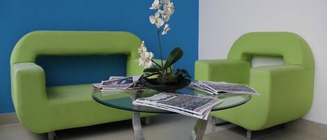 Un espace d’accueil avec deux canapés verts, une table en verre sur laquelle sont posés des journaux et une plante orchidée.