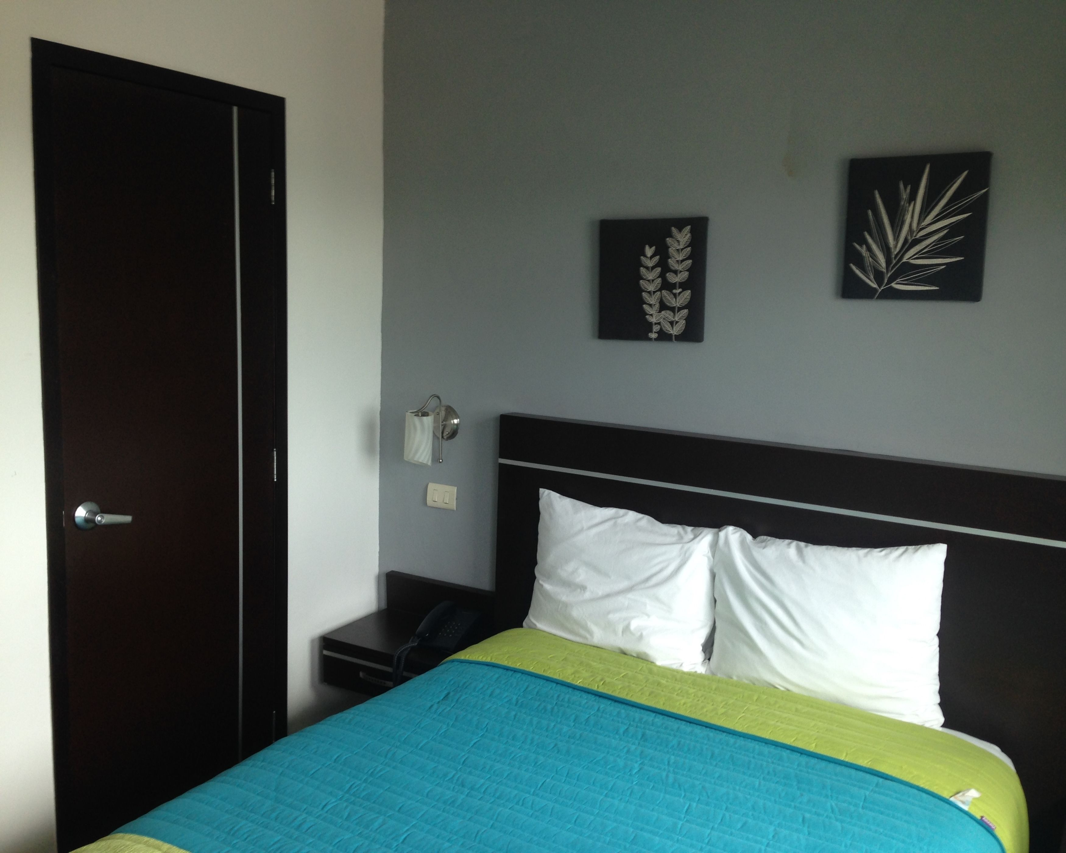 A hotel room with a bed, a nightstand, a lamp, and two wall art pieces.