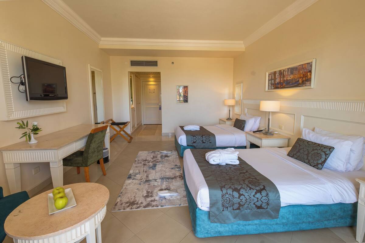 Une chambre d’hôtel avec deux lits, un bureau, une télévision et un tableau au mur.