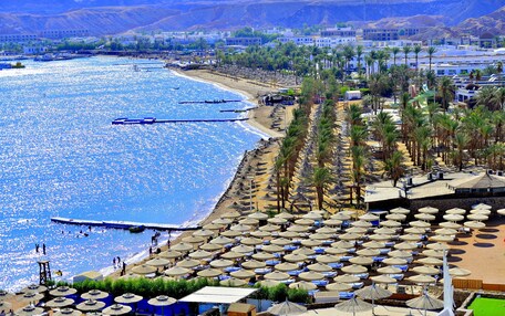 A beach resort with rows of umbrellas, a marina, and a backdrop of mountains.