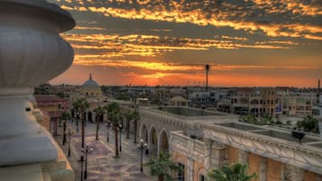 A historic building with arches and a dome, surrounded by palm trees and a paved plaza.