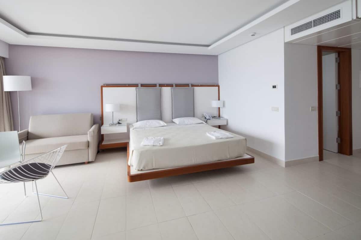 Una habitación de hotel moderna con una cama grande, un sofá, una silla y una mesita de noche con lámparas.