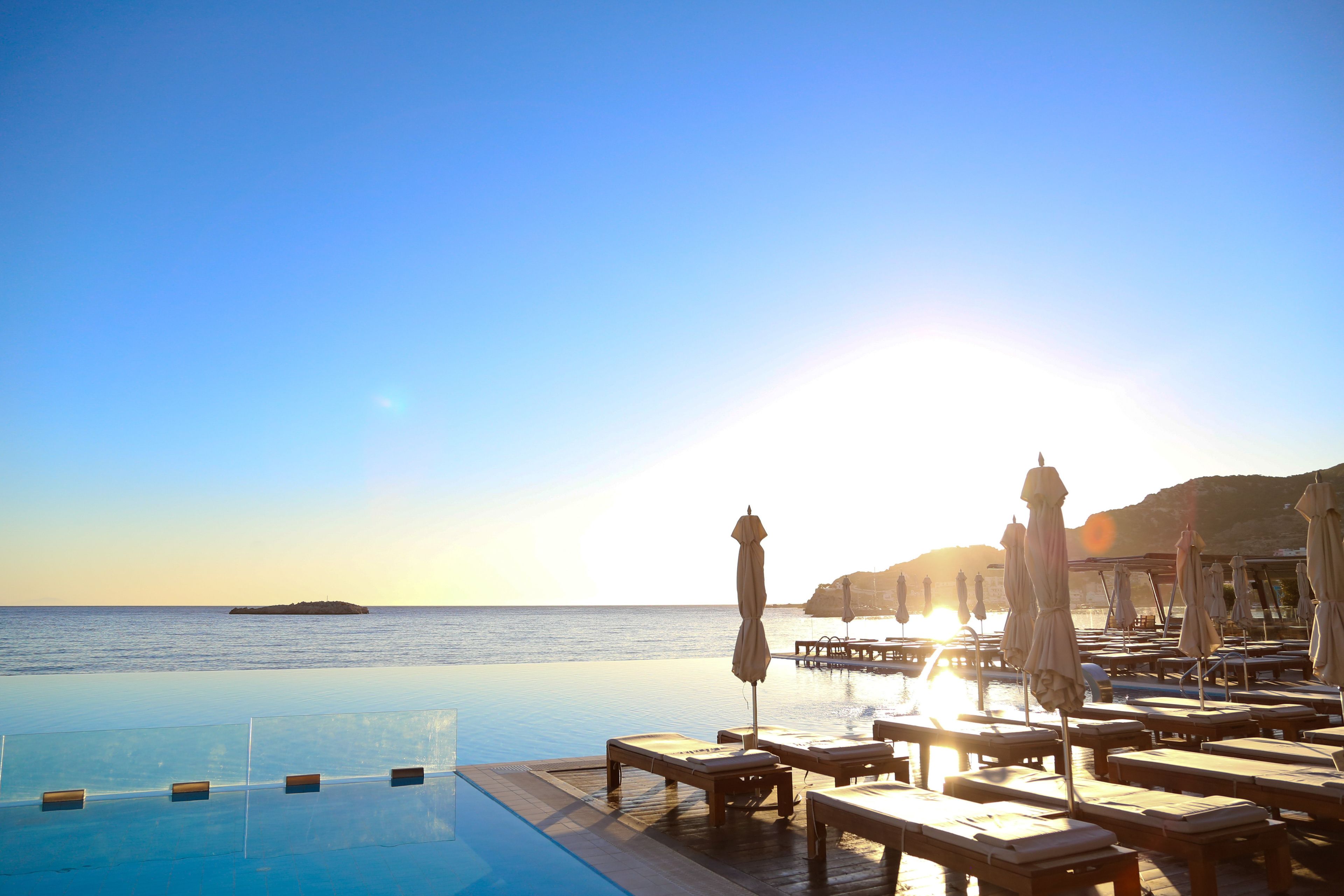 An infinity pool with lounge chairs and umbrellas, overlooking the sea and a distant island.