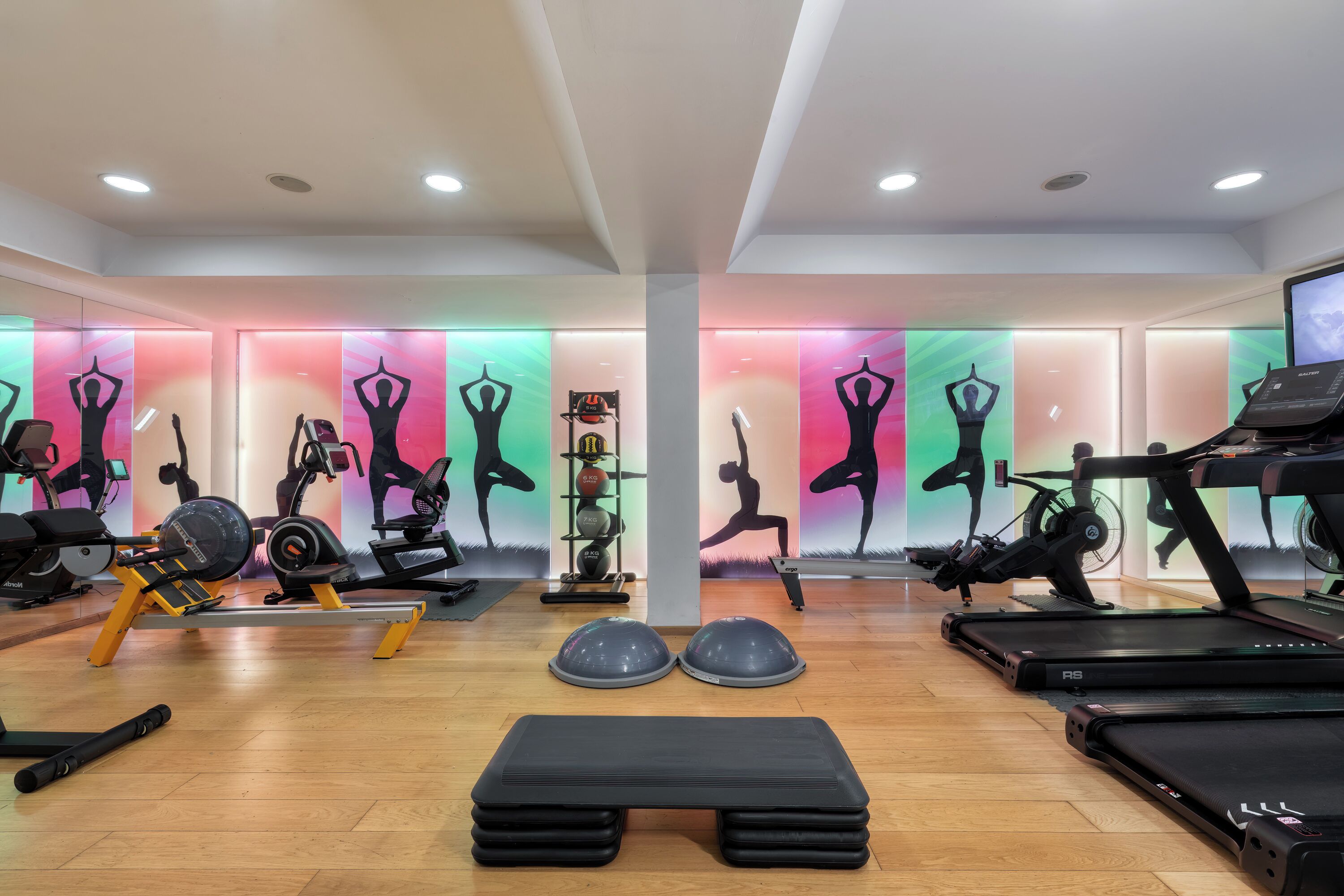 A gym with exercise equipment, a wooden floor, and colorful wall murals.