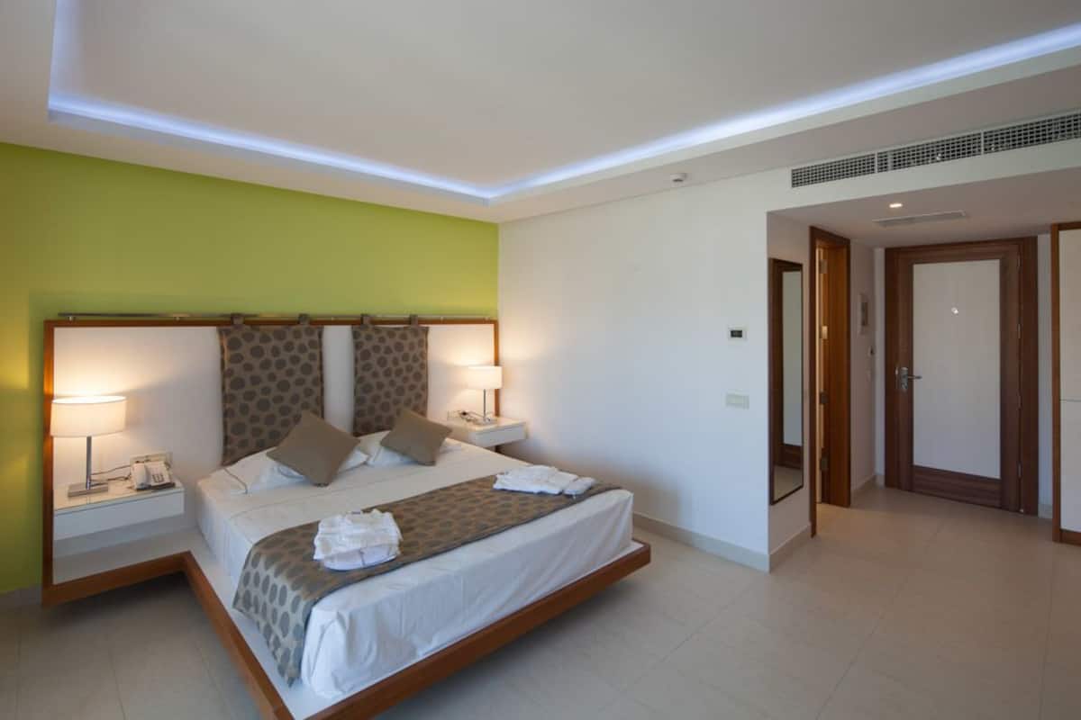 Una habitación de hotel moderna con una cama grande, dos mesitas de noche y una pared de acento verde.