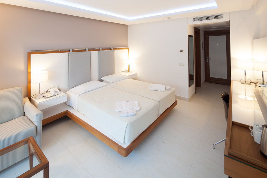 A modern hotel room with a large bed, bedside tables, a chair, and a desk with a lamp.