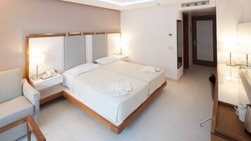 A modern hotel room with a large bed, bedside tables, a chair, and a desk with a lamp.