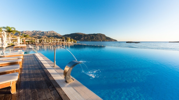 Una piscina con cascada, terraza de madera y sillones de descanso.