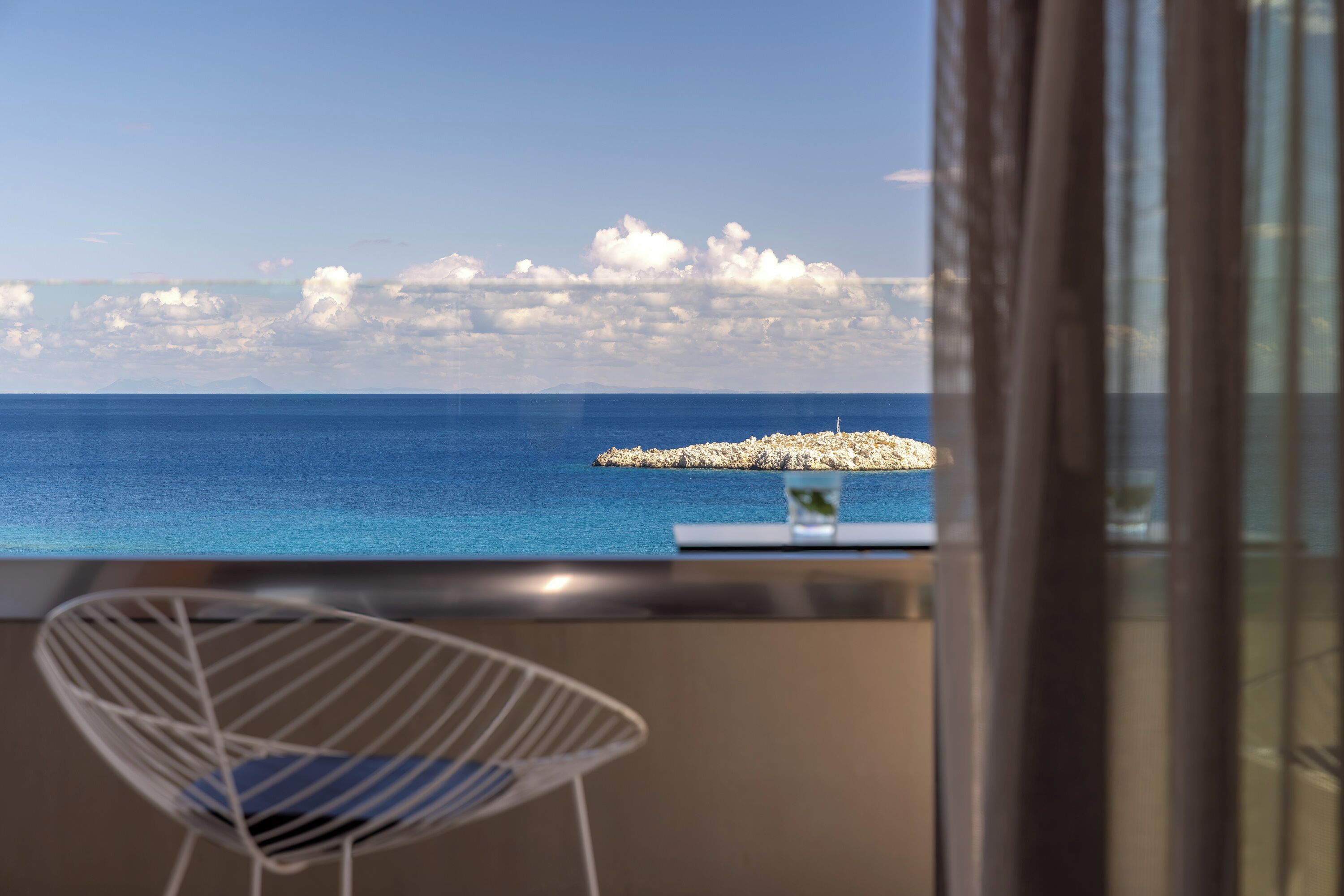 Une chambre avec vue sur la mer, une chaise et une petite table avec un verre.