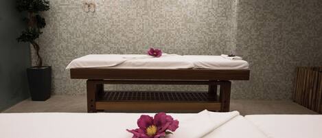 A spa room with a massage table, a potted plant, and a flower on the bed.