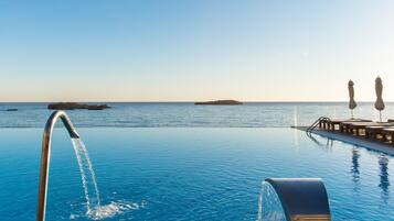 An infinity pool with a clear view of the ocean, a water fountain, and a deck with umbrellas.