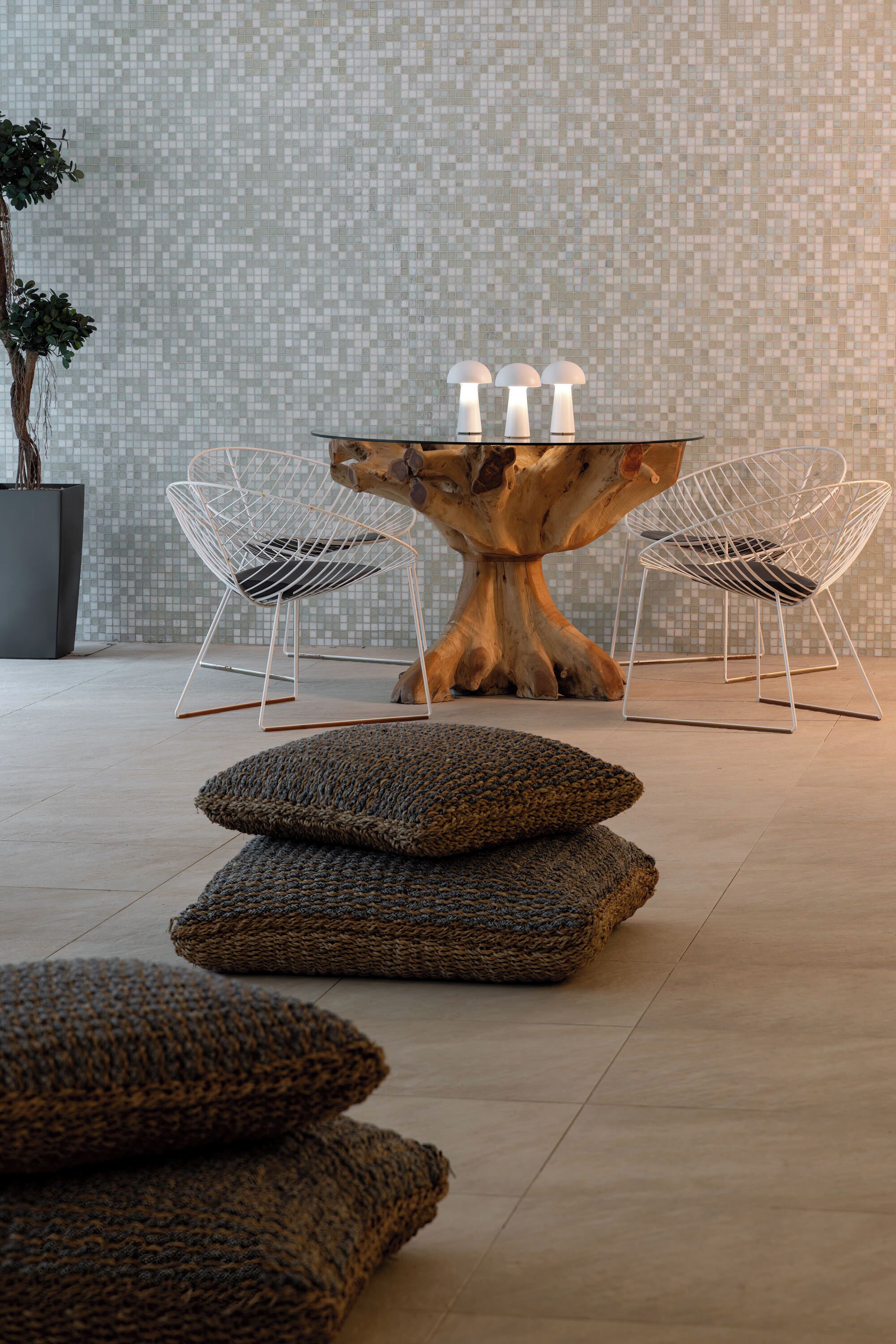 A modern interior with a central wooden table, two wireframe chairs, and a potted plant.