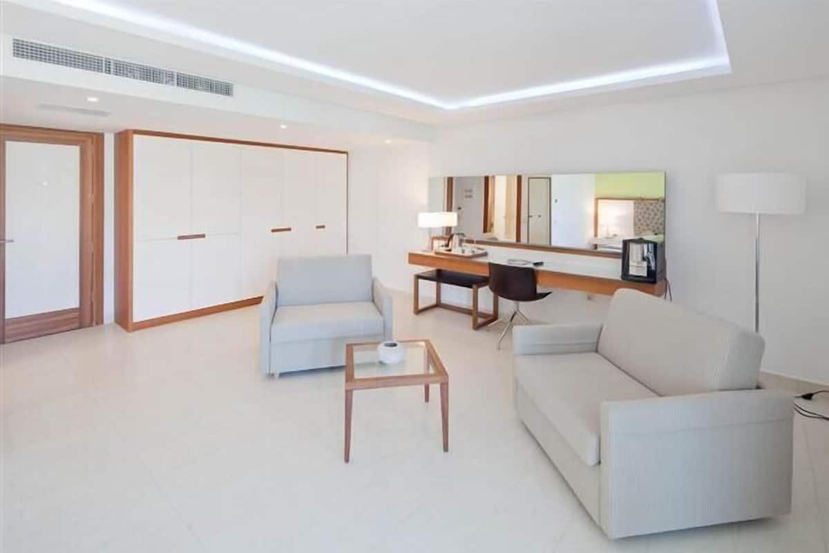 Una habitación de hotel moderna con sofá, sillón, escritorio y un espejo grande.