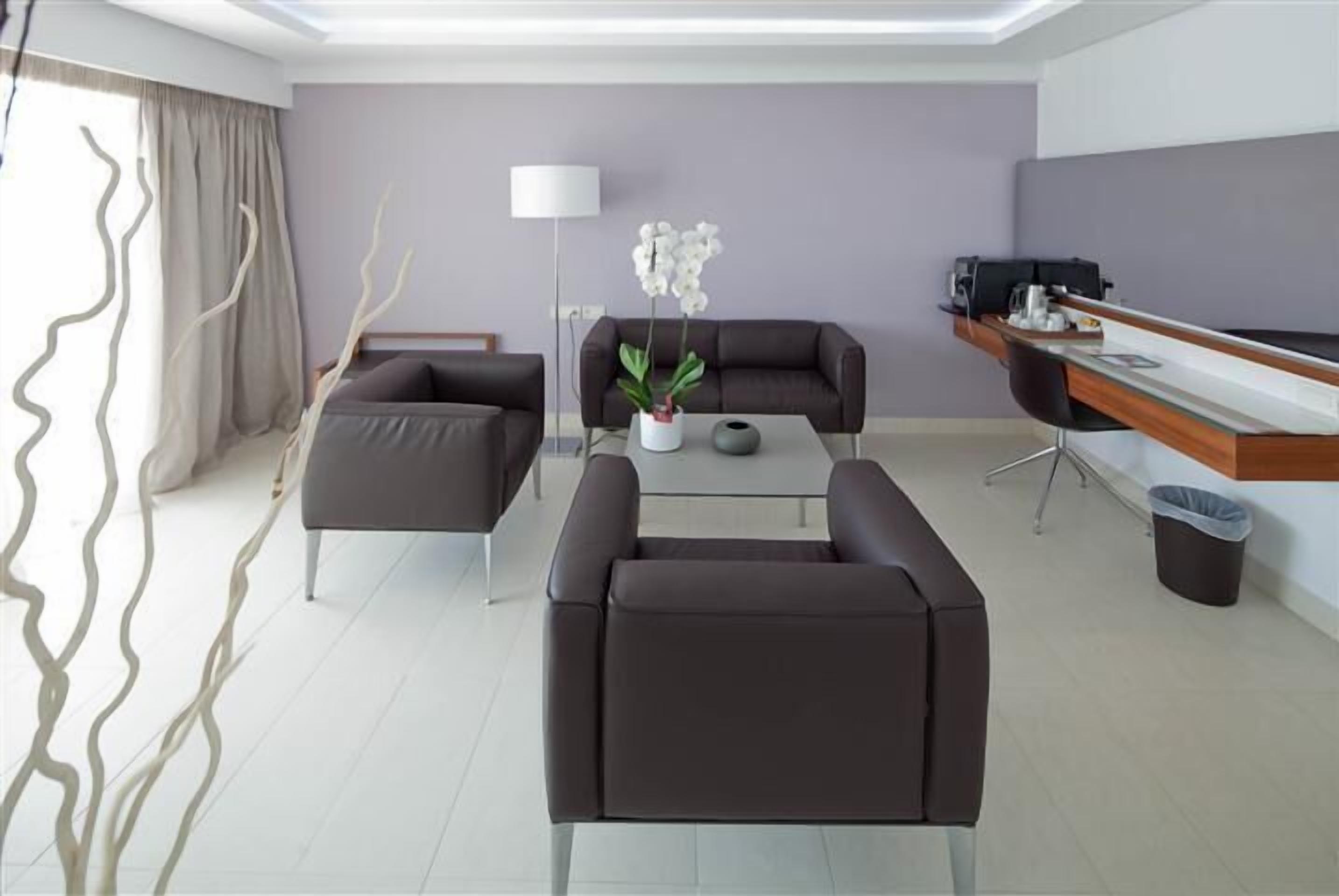 Un salon moderne comprenant un canapé, des fauteuils, une table basse, une lampe et un petit bureau avec un ordinateur.