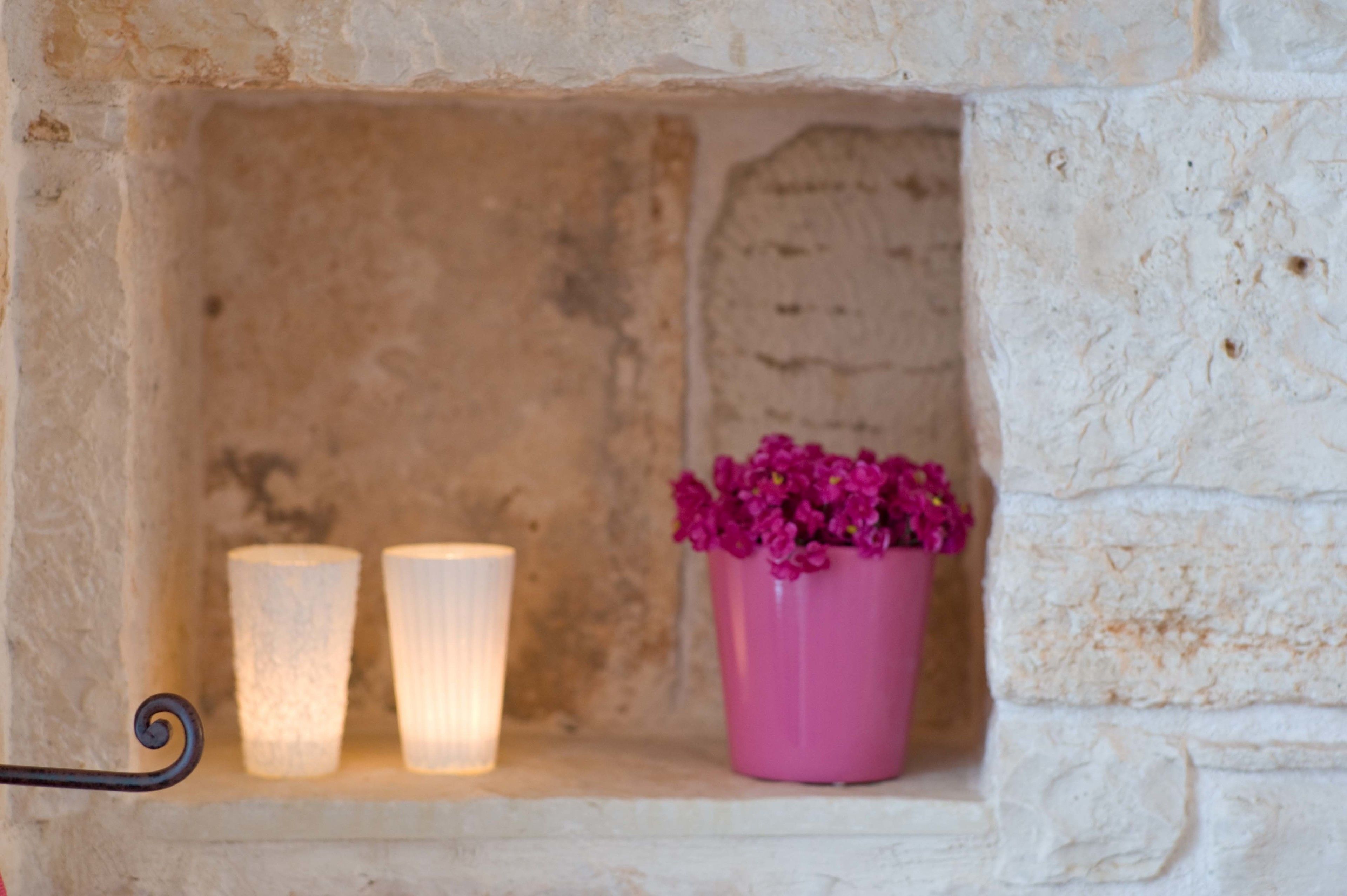 Ein Steinkamin mit zwei brennenden Kerzen und einer rosa Vase mit Blumen.