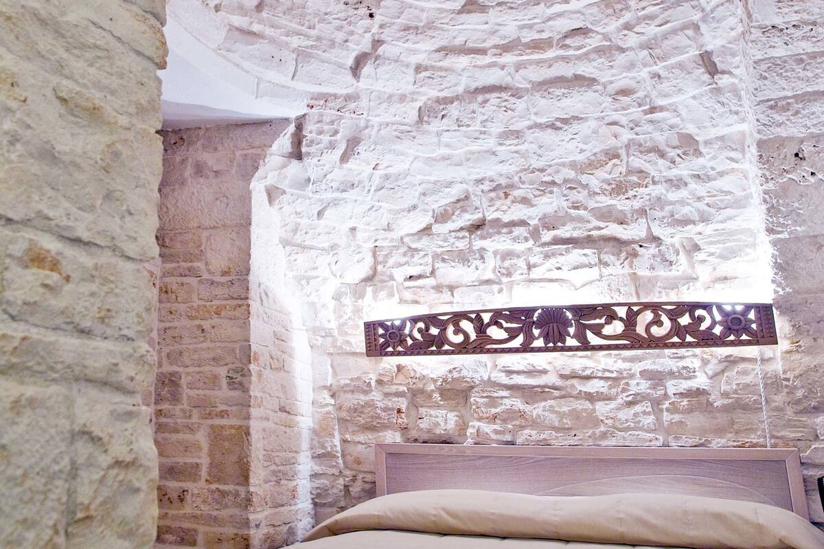 Une chambre avec un lit, des murs en pierre et une tête de lit en bois.