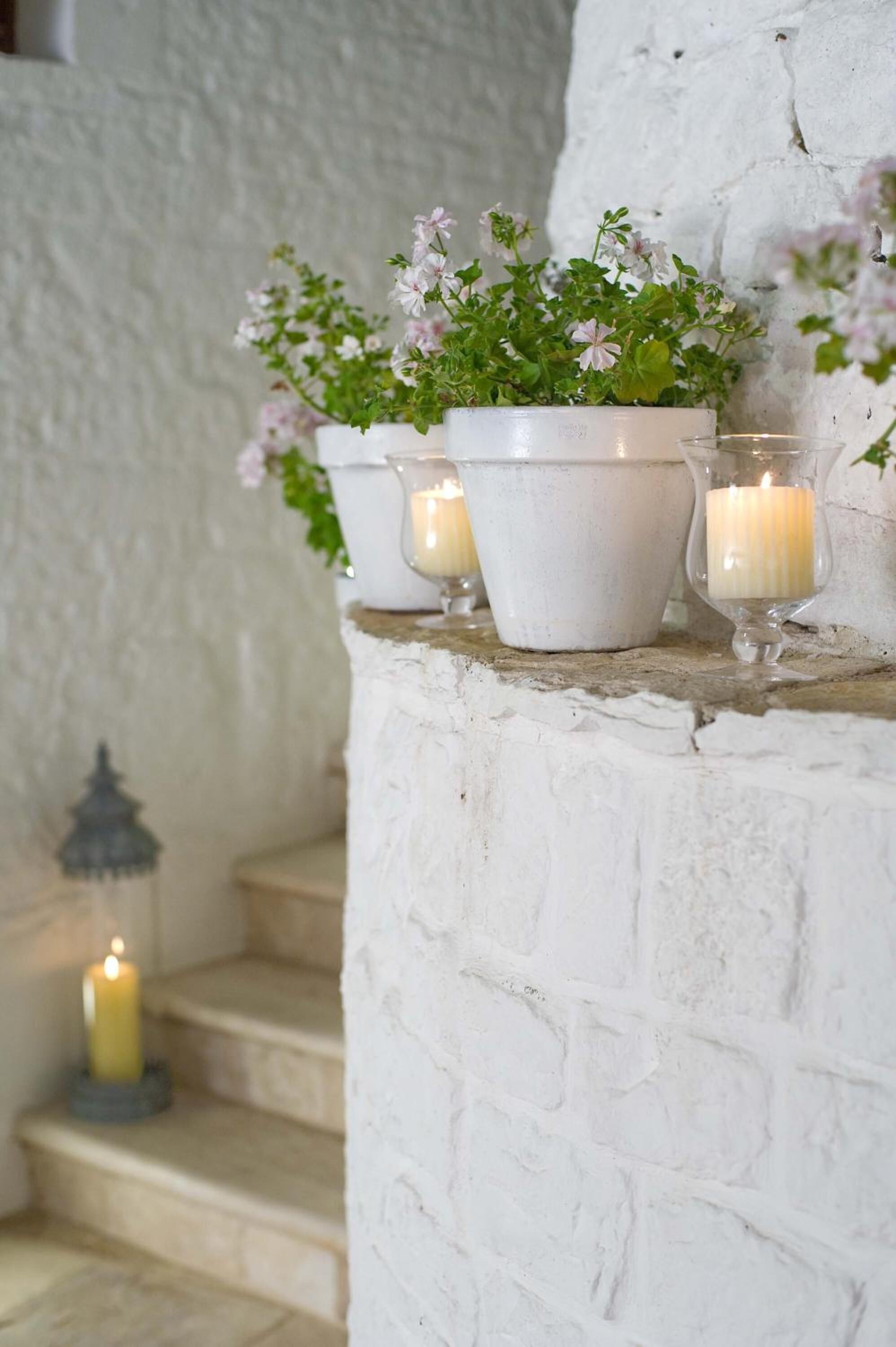 A white brick wall with a shelf holding potted plants and candles.
