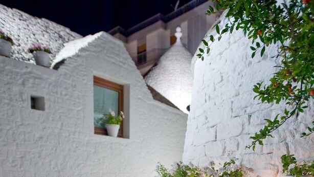 An outdoor seating area with a table and two chairs, surrounded by white stone walls and potted plants. - Le Alcove Luxury Resort nei Trulli (Alberobello)
