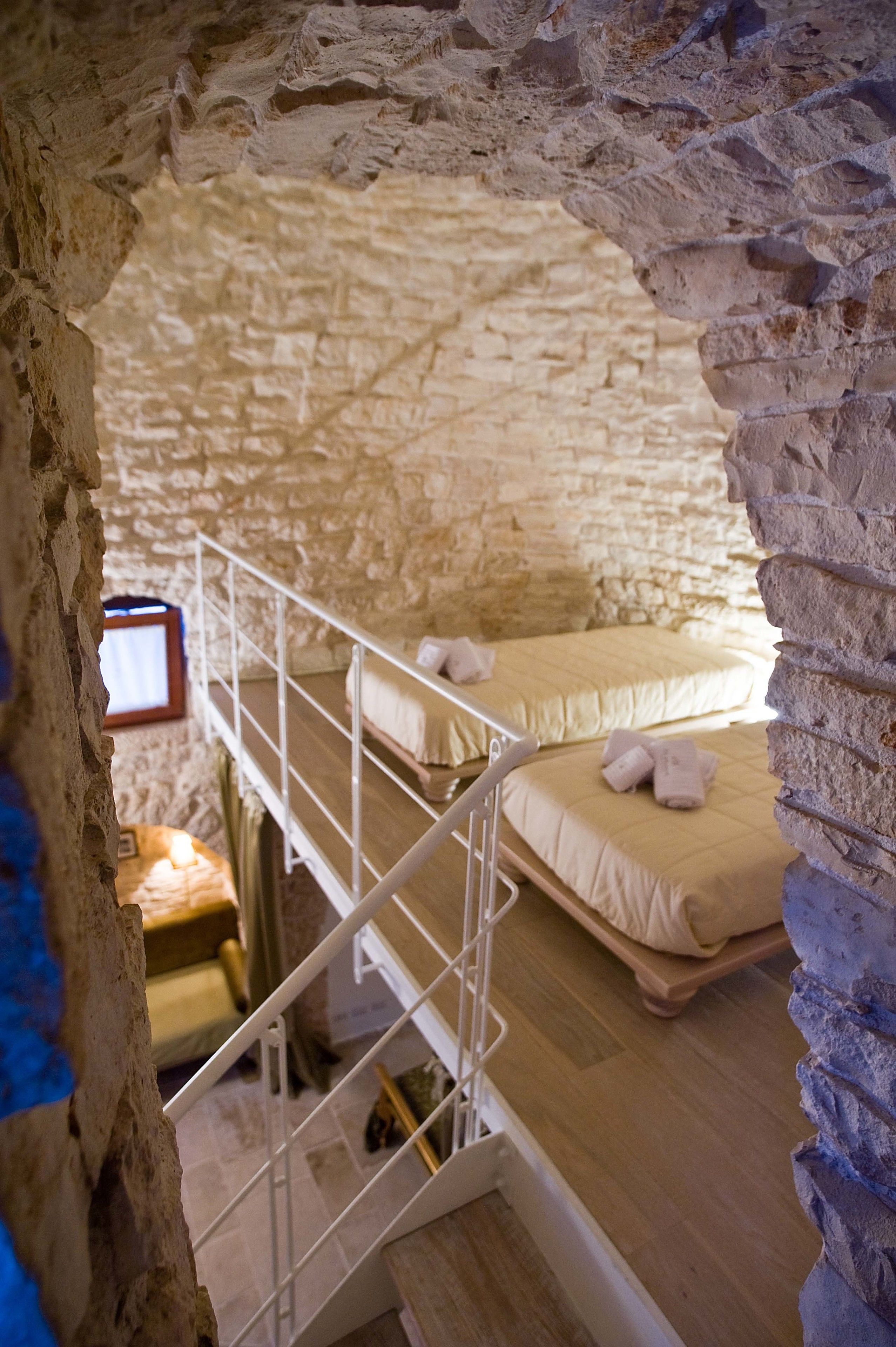 A stone-walled room with a bunk bed and a small desk with a computer.