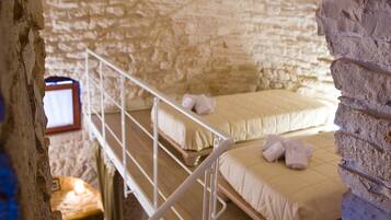A stone-walled room with a bunk bed and a small desk with a computer.