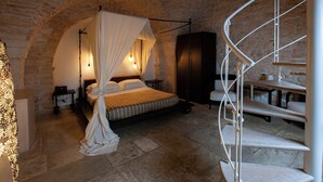A bedroom with a four-poster bed, stone walls, and a spiral staircase. - Le Alcove Luxury Resort nei Trulli (Alberobello)