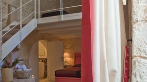 A spacious interior with a staircase leading to an upper level, a bench, and a basket with flowers. - Le Alcove Luxury Resort nei Trulli (Alberobello)