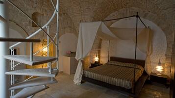 A bedroom with a stone ceiling, a bed with a canopy, a staircase, and a nightstand with a lamp.