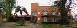 A two-story brick building with a curved facade, a stone entrance, and a small garden with palm trees.