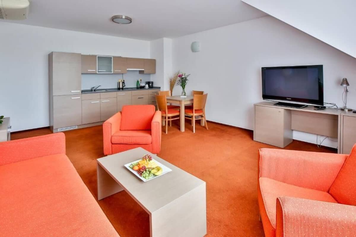Un espace de vie compact comprenant un coin cuisine, un coin repas et un espace détente avec des canapés orange et une table basse.