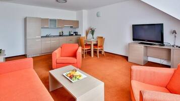 Un espacio habitable compacto con kitchenette, zona de comedor y sala de estar con sofás naranjas y una mesa de centro.
