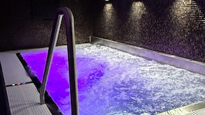 A spa area with a hot tub, tiled flooring, and wall-mounted lights.
