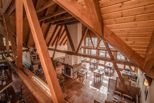 Un interior espacioso con altos vigas de madera, chimenea y múltiples zonas de comedor con mesas y sillas.