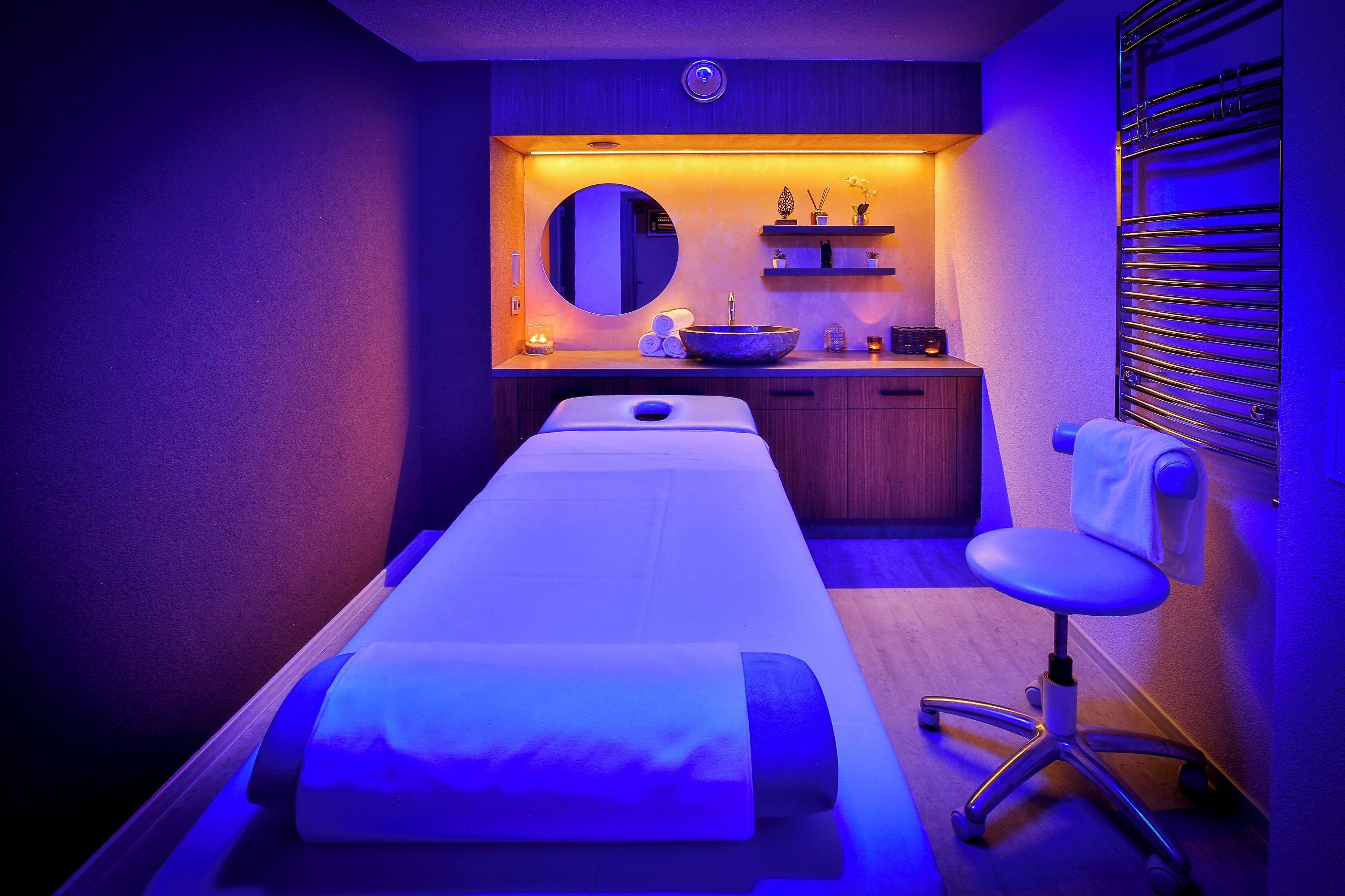 Et massageværelse med massagestue, en stol, en vask og et spejl.