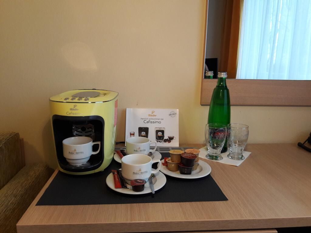 Habitación de hotel con cafetera, tarjeta para el servicio de café, una botella de agua y un vaso sobre la mesa.