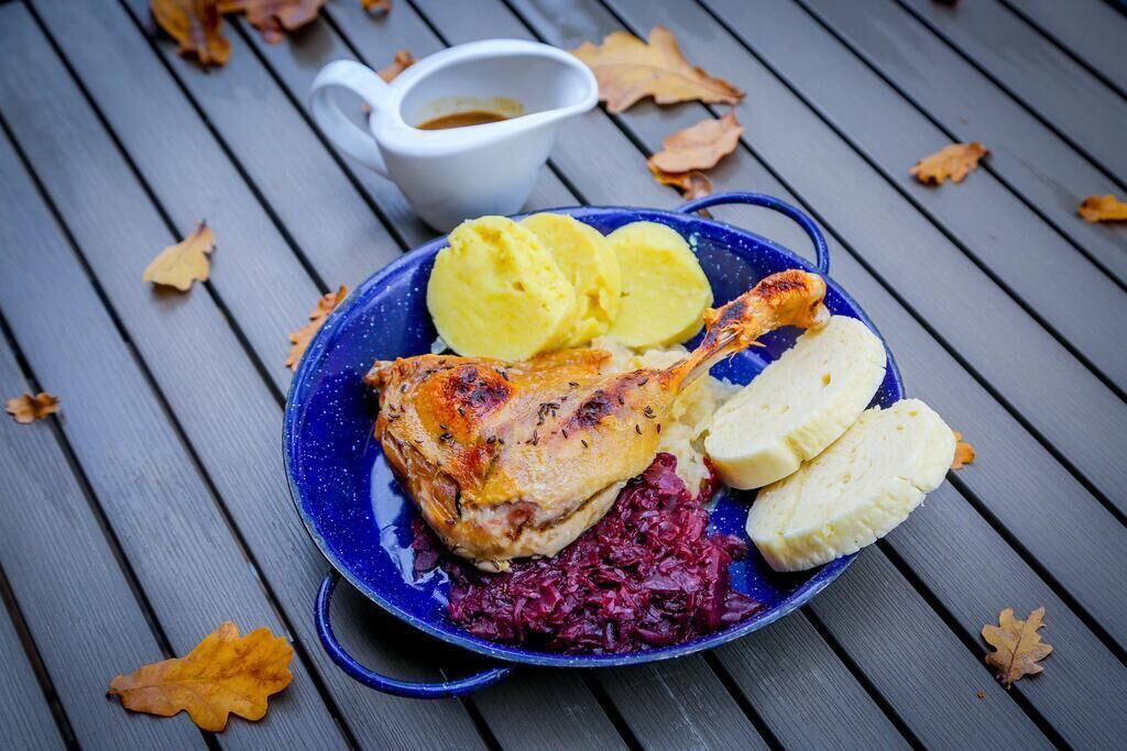 Ein Teller mit gebratenem Hähnchen, gekochten Kartoffeln und Rotkohl, dazu eine kleine Schüssel Sauce.