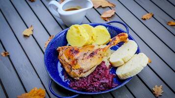 Ein Teller mit gebratenem Hähnchen, gekochten Kartoffeln und Rotkohl, dazu eine kleine Schüssel Sauce.