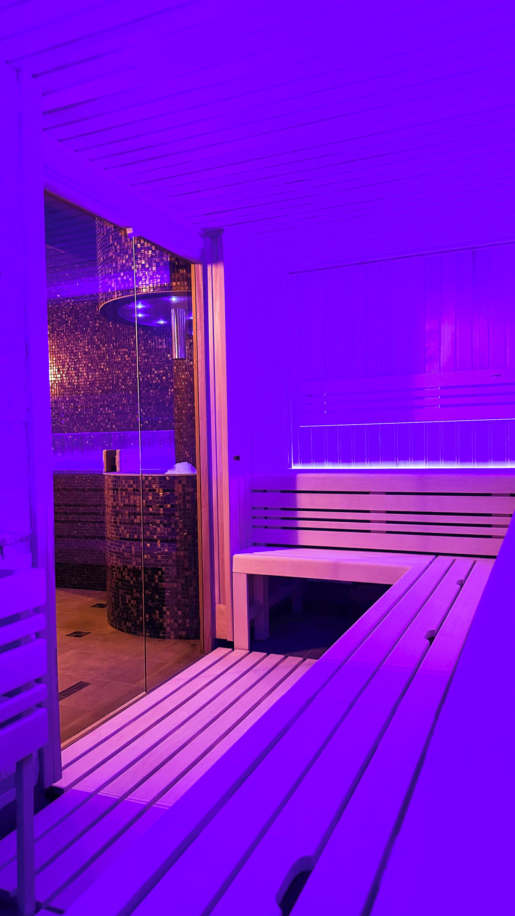 Ein modernes Interieur mit einer sitzecke in violettem Licht und einer Glaswand mit Mosaikmuster.