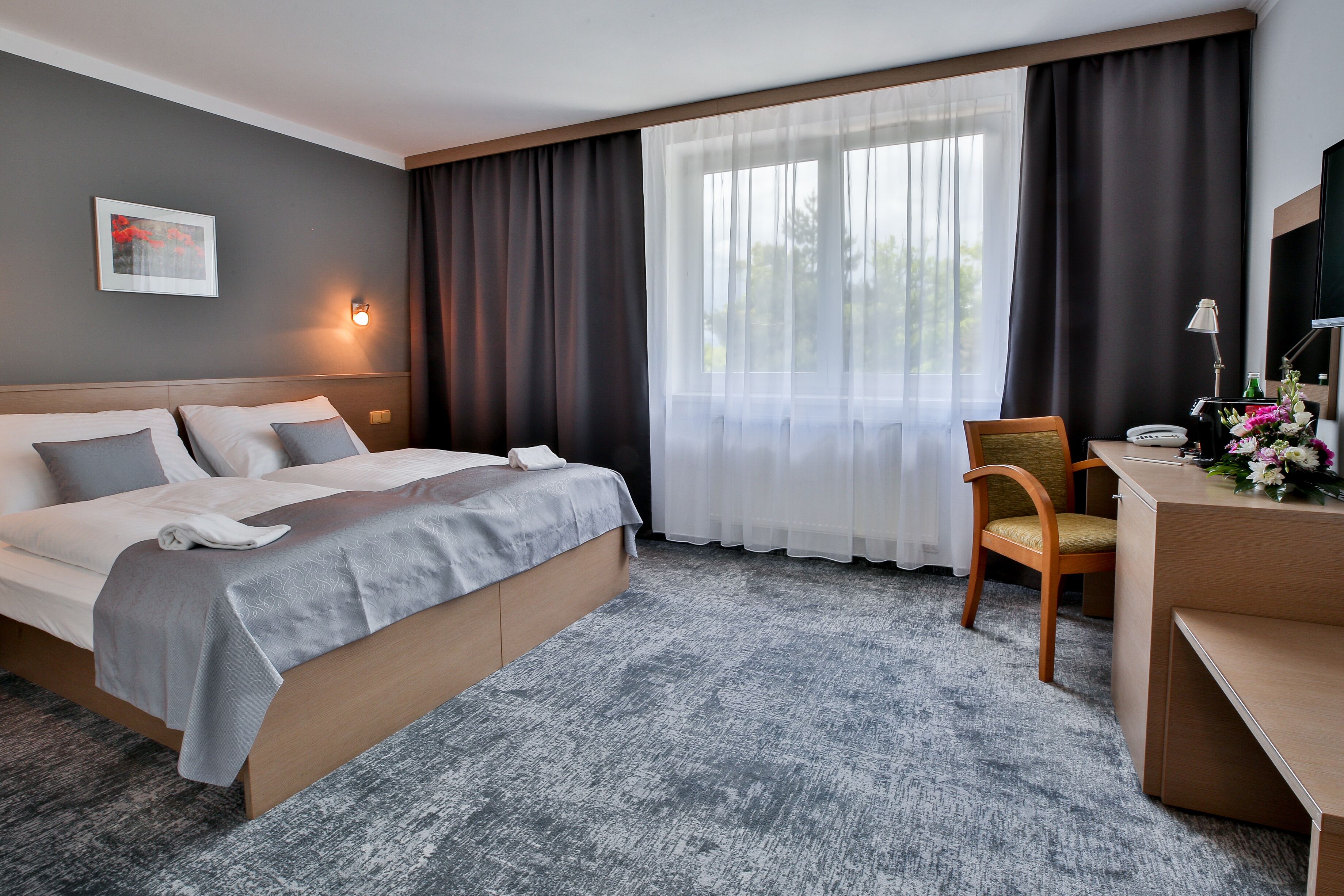 Habitación de hotel con cama, escritorio, silla, lámpara y ventana con cortinas.