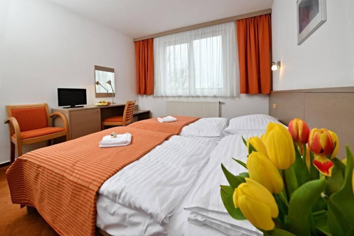 Une chambre d’hôtel avec un lit, un bureau avec un ordinateur, une chaise et une fenêtre avec des rideaux.