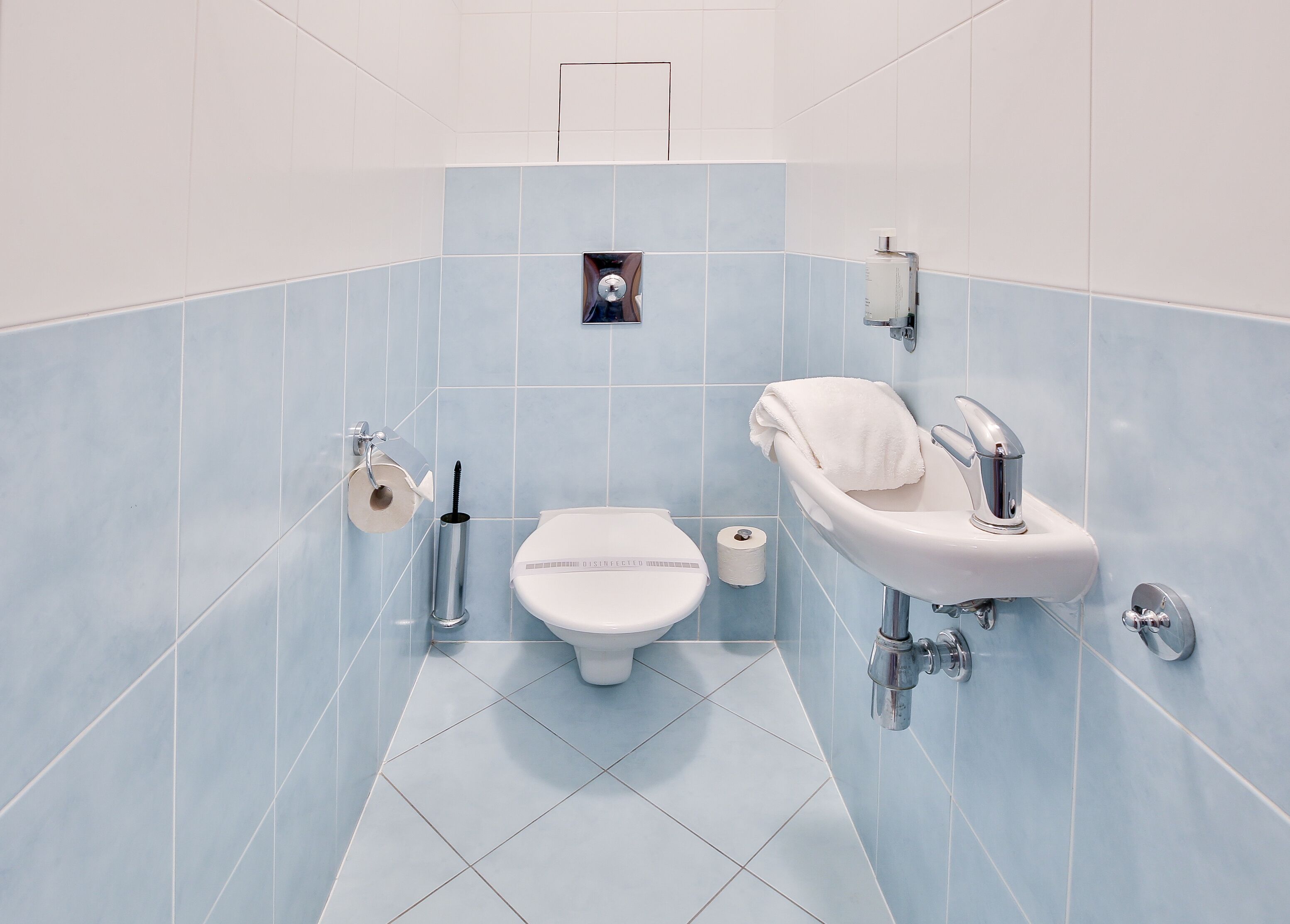 A modern bathroom with a toilet, sink, and toilet paper dispenser.