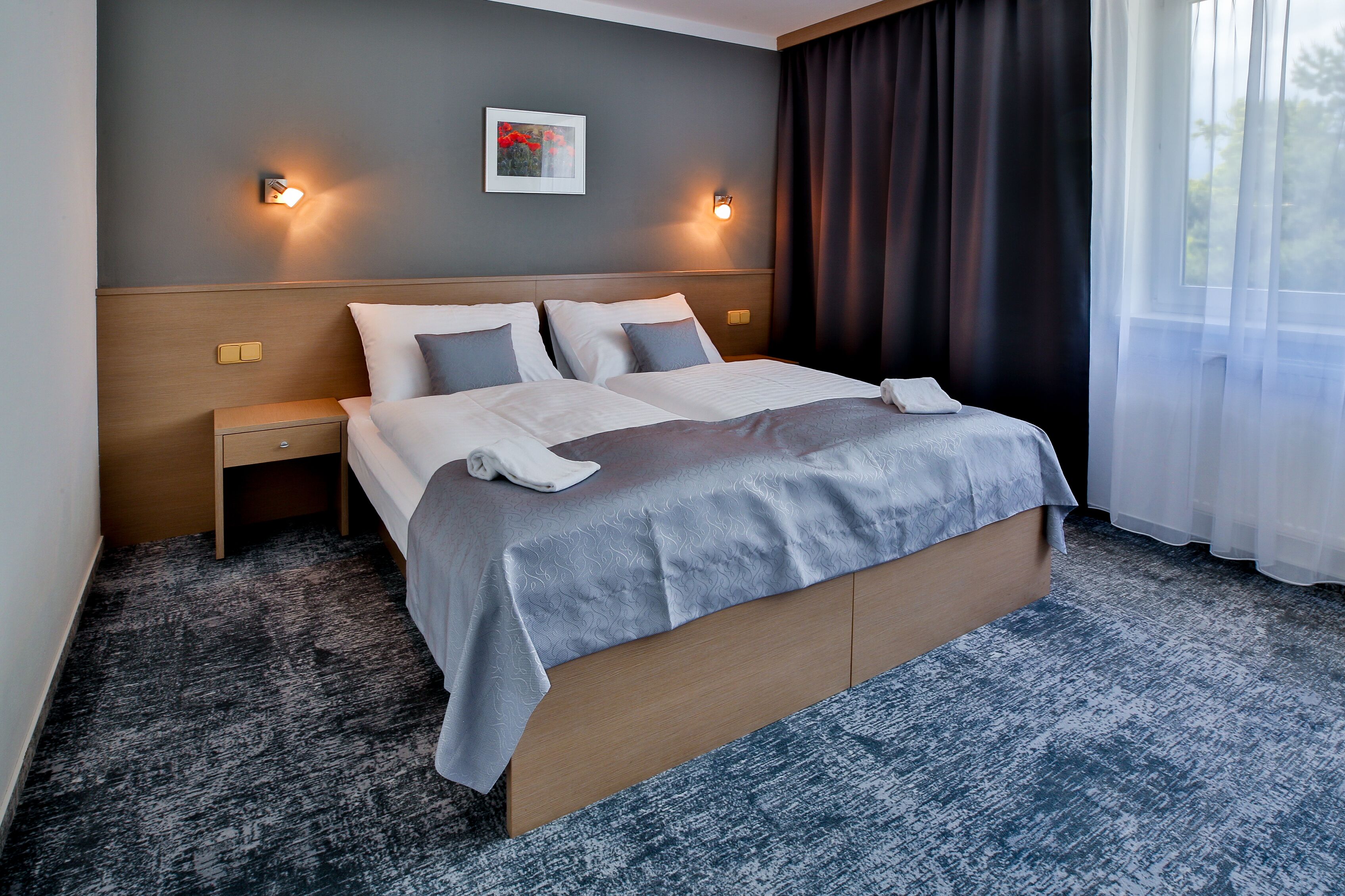 Ein Hotelzimmer mit einem großen Bett, zwei Nachttischen, einer Ablage, einer Wandleuchte und einem Fenster mit Vorhängen.