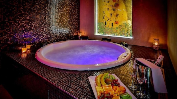 A spa tub with a mosaic tile wall, a painting, and a fruit platter with glasses.