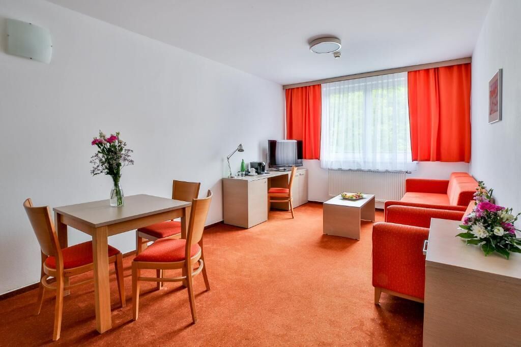 A compact living space with a dining area, a kitchenette, a TV, and a seating area with red furniture.