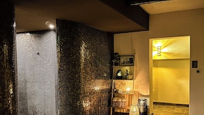 A modern interior with a mosaic wall, a wooden shelf with decorative items, and a warm-lit hallway.