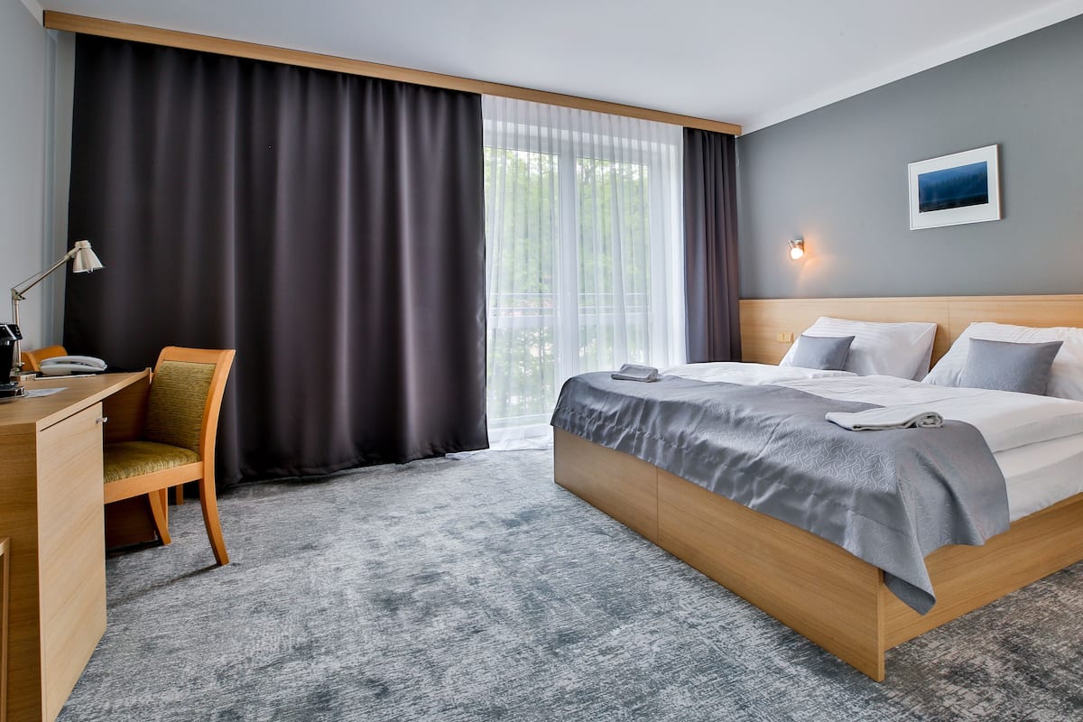 Une chambre d’hôtel avec un lit, un bureau, une chaise et une fenêtre avec des rideaux.