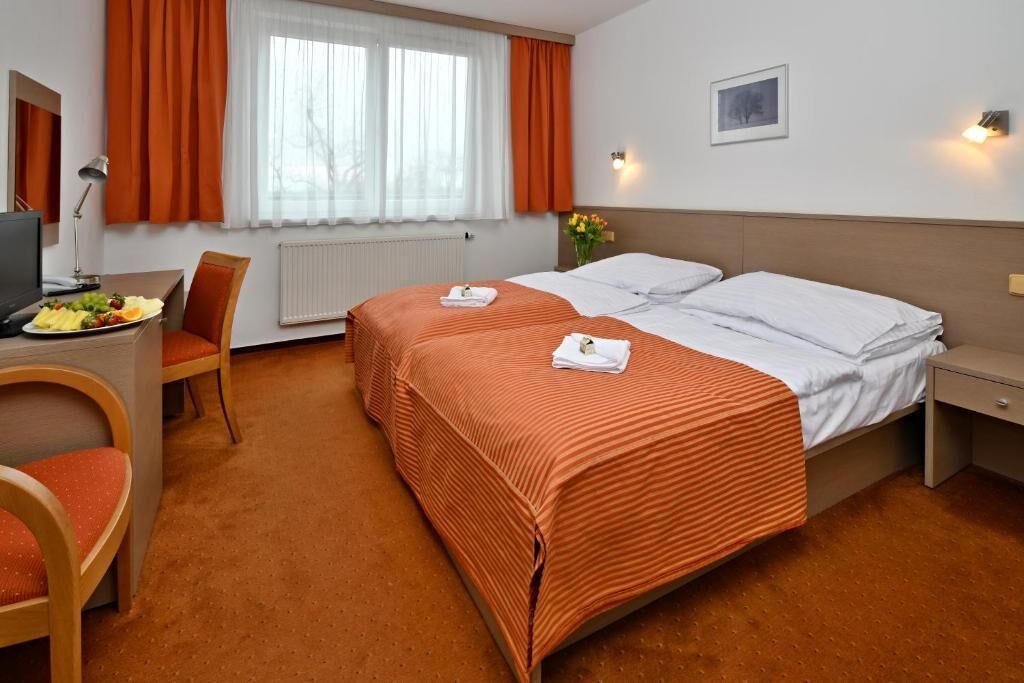 Habitación de hotel con dos camas, un escritorio, una silla, un televisor y una ventana con cortinas.