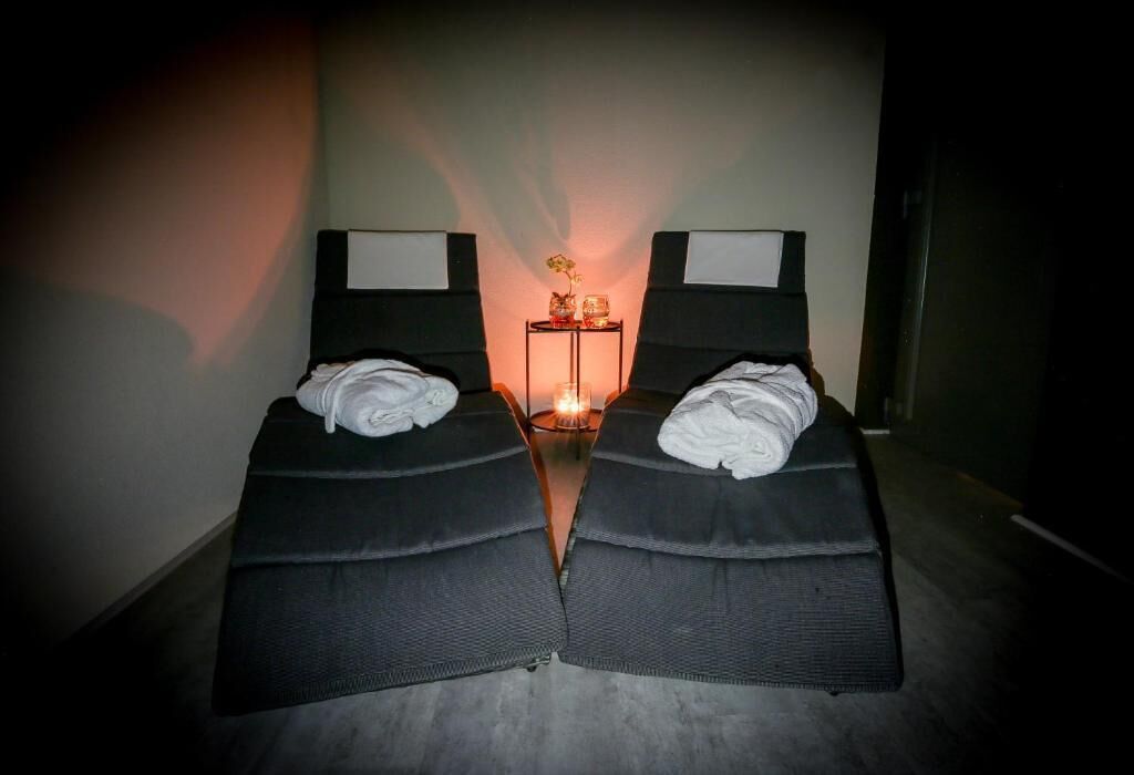 Dos camas individuales con cabeceros oscuros y ropa de cama blanca, una mesita de noche con lámpara y un pequeño objeto decorativo sobre la mesa.