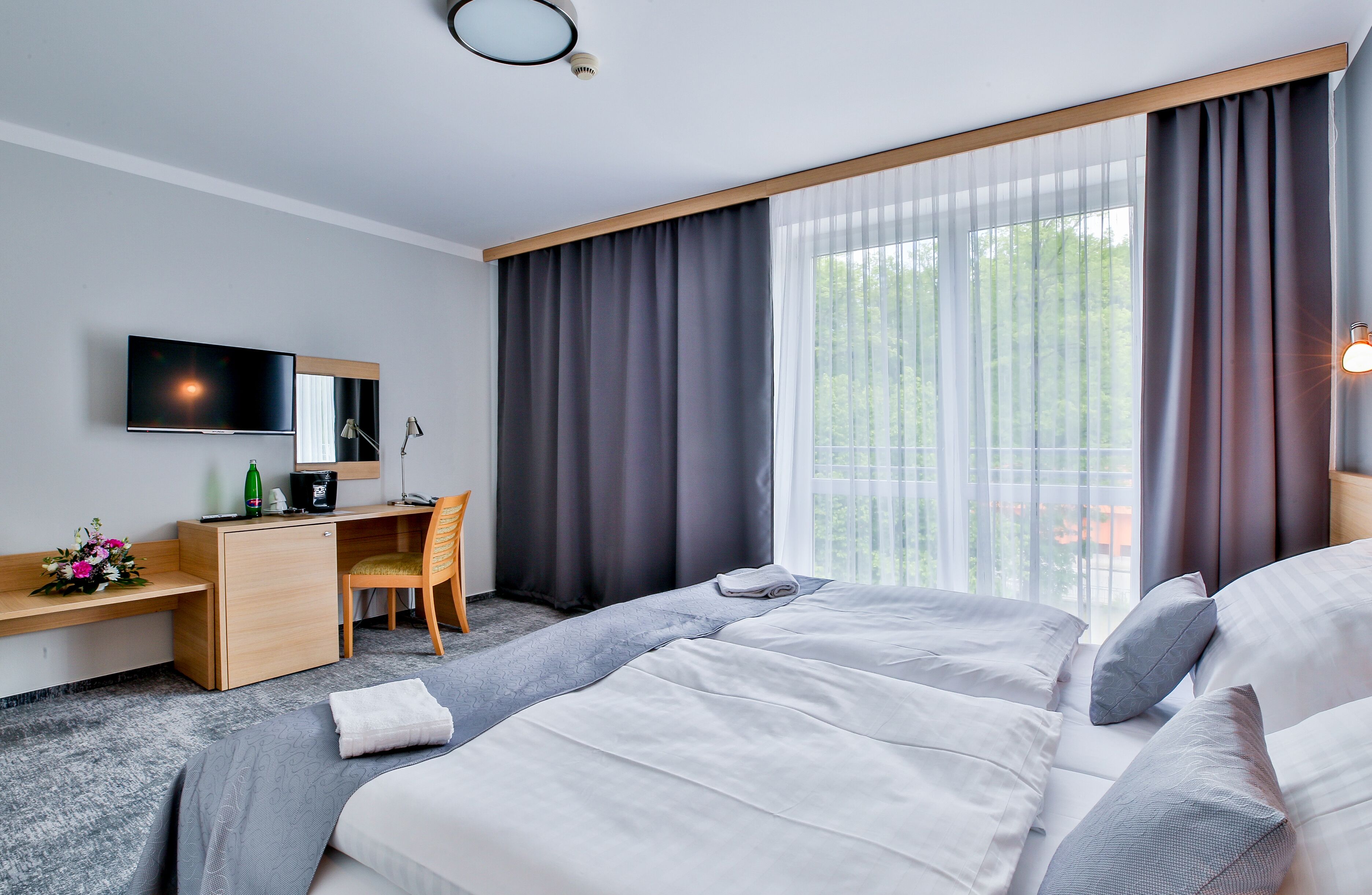 Habitació d'hotel amb un llit, escriptori amb ordinador, televisió i finestra amb cortines.